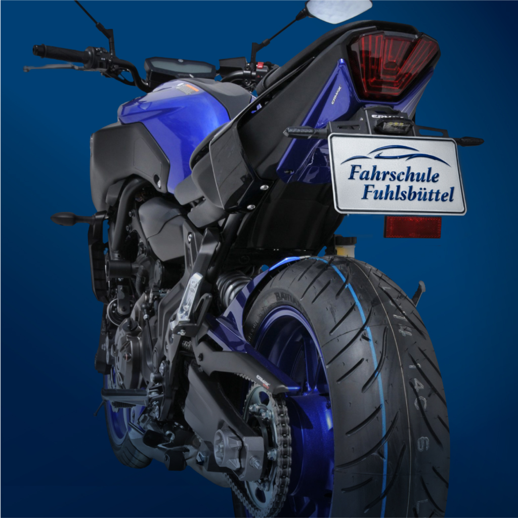 Motorrad von hinten fotografiert, mit sichtbarem Hinterrad, Auspuffanlage und Kennzeichenhalter. Das Motorrad steht auf einem dunkel gehaltenen Untergrund.